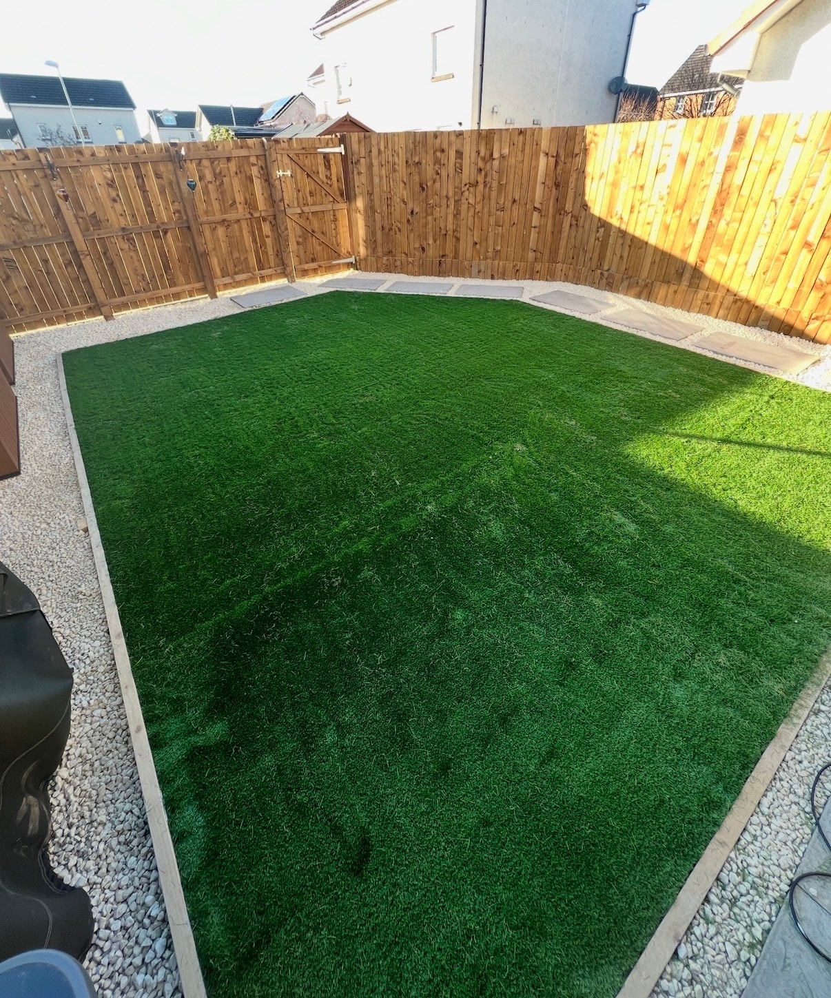 Artificial grass back garden with timber edging and white gravel border